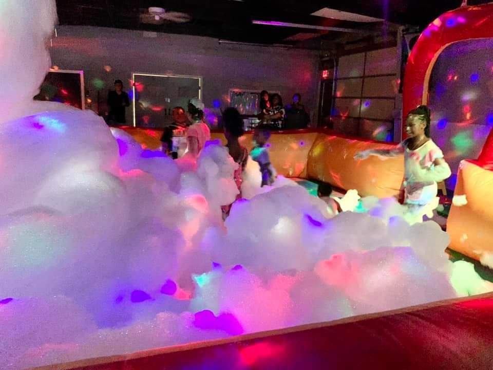 Kids play in party foam as colorful lights bounce off the foam