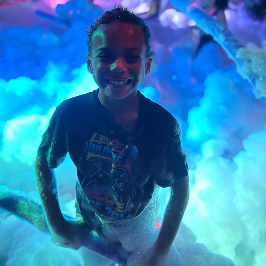 A happy child covered in party foam, with party foam behind him