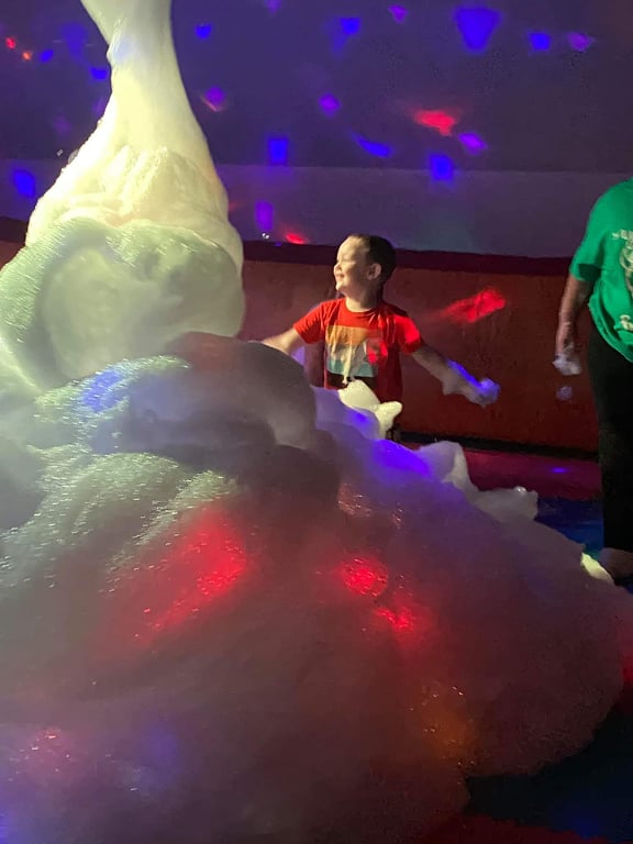 A child smiles behind a mound of party foam taller than the child.