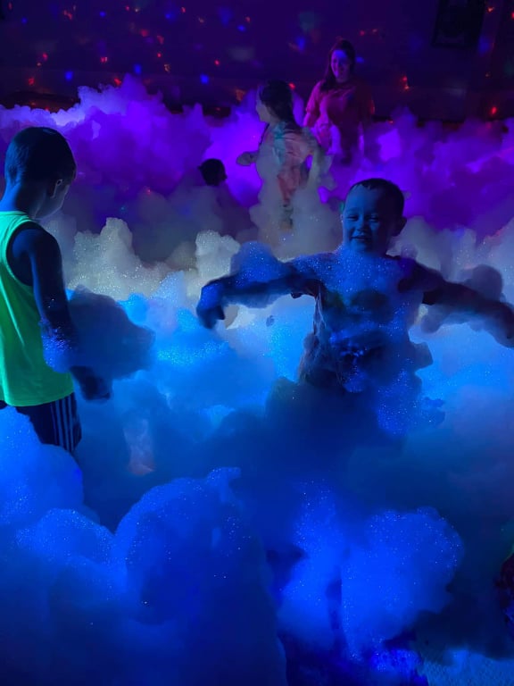 A group of children play in waist-deep party foam. One child is covered in party foam.